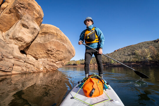 senior male is paddling stand up paddleboard along sandstone cliff on Horsetooth Reservoir in northern Colorado - POV