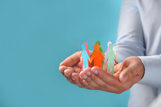 Hands holding colorful paper people cutouts on a light blue background symbolizing diversity and inclusivity with diversity inclusivity community together
