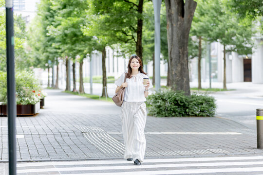 コーヒーを片手にオフィス街を歩く日本人女性