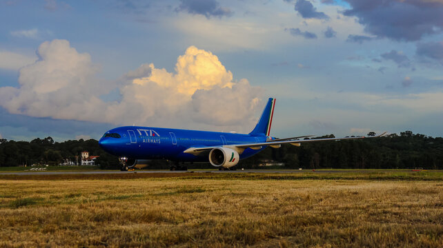 Avi&atilde;o da ITA Airways taxiando no Aeroporto Internacional de Guarulhos, com pista, gramado, vegeta&ccedil;&atilde;o e c&eacute;u carregado. Guarulhos, SP, 22 de julho de 2026.