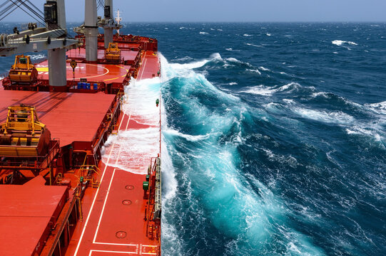 Red cargo ship sailing through rough sea waves