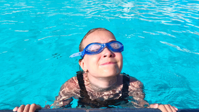 Young girl wearing swimming goggles in a clear blue pool on a sunny summer day. Perfect for themes of childhood, swimming lessons, family vacations, water sports, and healthy outdoor activities.