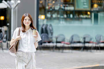 Fototapeta premium テイクアウトコーヒーを持って街を歩く日本人女性