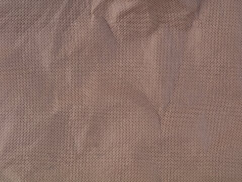 Close-up full frame shot of a brown non-woven synthetic fabric texture with slight wrinkles and creases, creating a textured background template for design, clothing, or packaging concepts