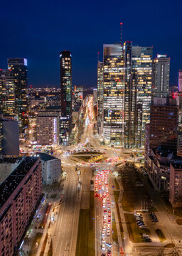 Aerial view of the illuminated skyscrapers and busy urban traffic at the Rondo ONZ roundabout in the city center of Warsaw at night, Poland.