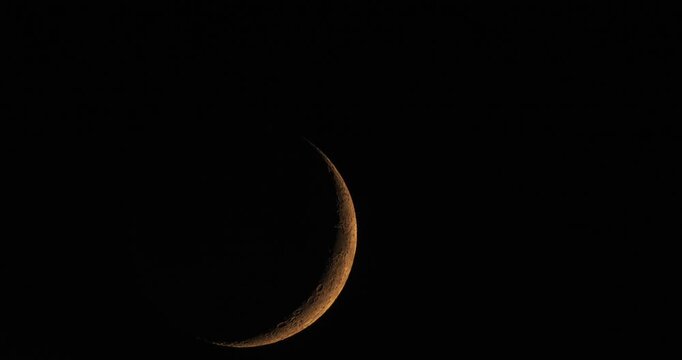 Panoramic time-lapse shot of a young crescent moon setting in the pitch black night sky with copy space.
