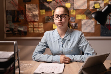 Obraz premium A disgruntled female detective puffs out her cheeks and expresses dissatisfaction while working with evidence in an office at night.