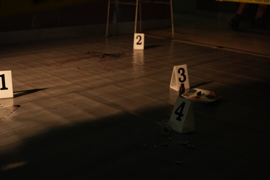 Forensic evidence markers and a bloody knife document the floor of a crime scene cordoned with yellow police tape during investigation.