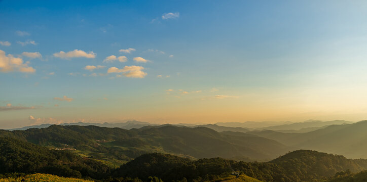 Mountain landscape at golden hour with rolling hills and soft sunlight under blue sky