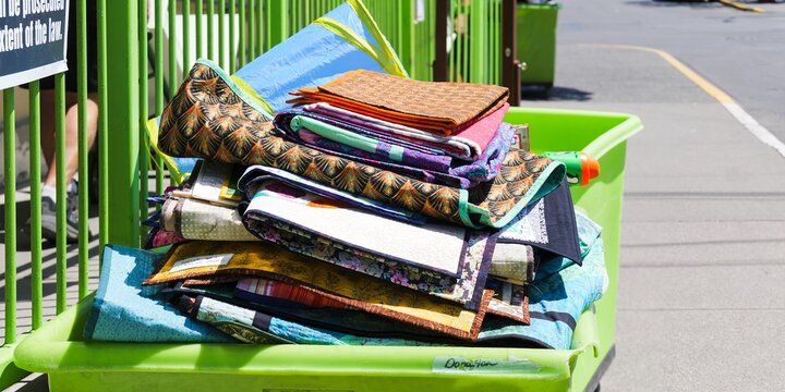 Colorful quilts stacked in a green bin under bright sunlight. Donation concept