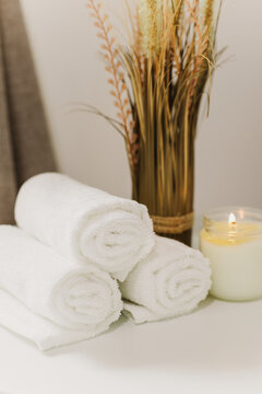 Minimalist still life of luxury spa essentials. White cotton towels with candle on a table.