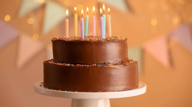 Two tier chocolate birthday cake with colorful lit candles and festive sprinkles celebration dessert