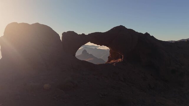 Stunning aerial view of the Arco del Aserrador, a natural stone arch, framing the famous Roque Bentayga monolith at sunrise in Gran Canaria