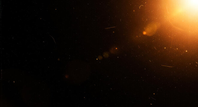 A dark background is illuminated by a bright, warm light source, creating a scattering of golden sparks and streaks.