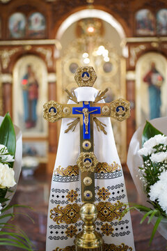 Golden church cross with blue details on an embroidered towel before the iconostasis during a wedding ceremony.