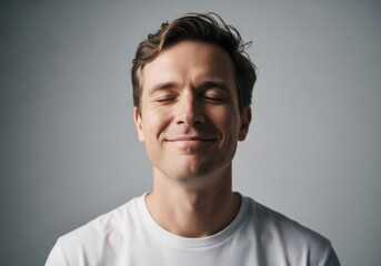Obraz premium Portrait of a serene young man with closed eyes, expressing peace and contentment against a neutral grey studio background
