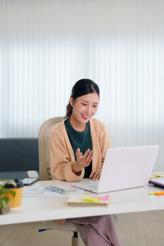 Young Asian professional woman conducting video call meeting with laptop at modern home office workspace
