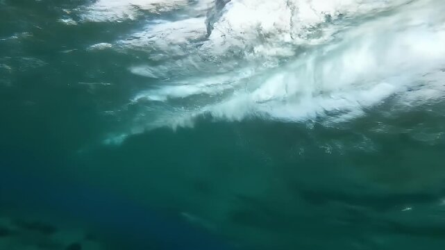 Underwater view of a breaking wave with sunlight filtering through the water