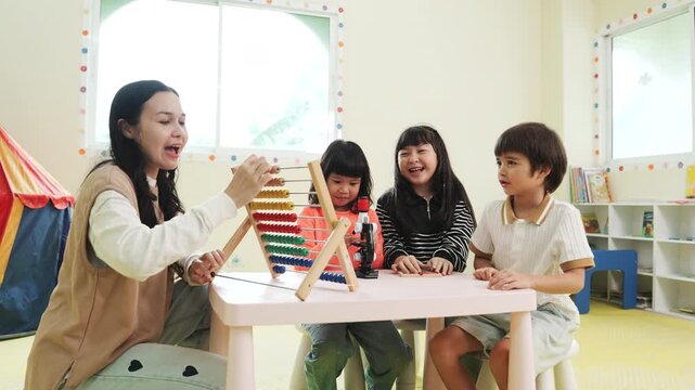 Teacher teaching children math with an abacus in kindergarten class. Asian kids learning and playing with educational toys in preschool daycare room, early childhood development.