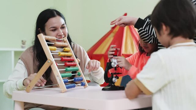 Teacher teaching children math with an abacus in kindergarten class. Asian kids learning and playing with educational toys in preschool daycare room, early childhood development.