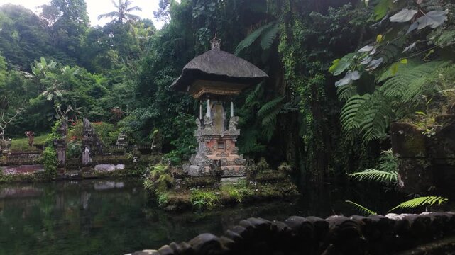 Small Balinese Hindu pelinggih shrine sit's on the water with a backdrop of jungle and crystal clear water. Camera tracks across. Location: Pura Gunung Kawi Sebatu Water Temple, Ubud, Bali.