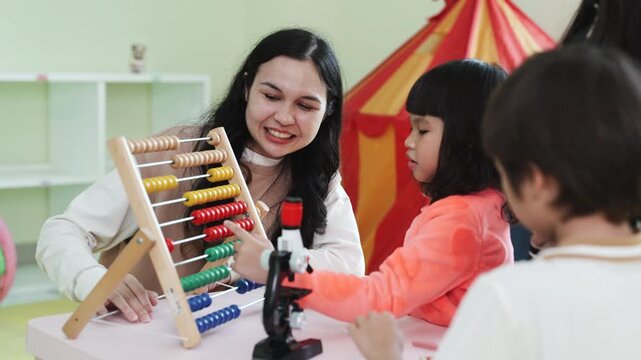 Teacher teaching children math with an abacus in kindergarten class. Asian kids learning and playing with educational toys in preschool daycare room, early childhood development.