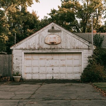 straight on view of a backyard garage that has a hoop on it. show the short driveway or pavement in front of the garage as well.