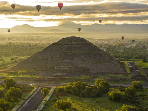 Aerial view of the Pyramid of the Sun at Teotihuacan with hot air balloons floating in the golden morning light over the ancient archaeological site, Mexico.