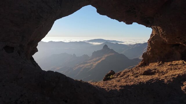 Beautiful panoramic view of a mountain range seen through the Arco del Aserrador, a natural stone arch, during a sunny day in Gran Canaria