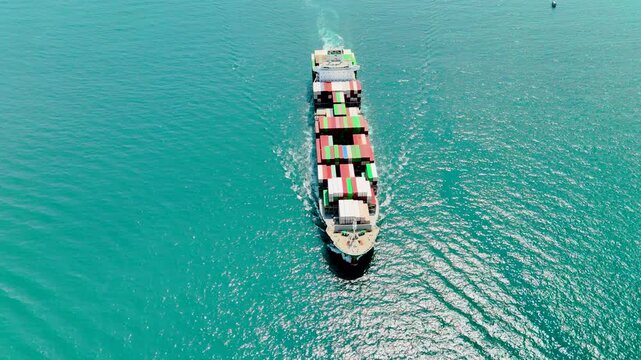 A large green container ship sails toward its destination, viewed from above. Cargo transportation concept
