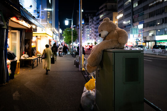 A stuffed teddy bear on a city street at night in Tokyo, Japan.