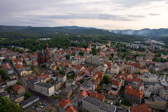 Aerial panorama of Walbrzych historic town in Lower Silesia, Poland at sunrise. The historic center with neogothic church and red-roofed buildings is surrounded by green hills and Sudeten mountains.