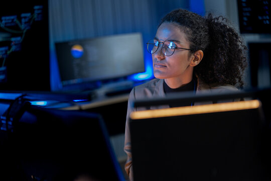 Black female cybersecurity expert examines data visualizations on a holographic-style display in a dark AI innovation lab.