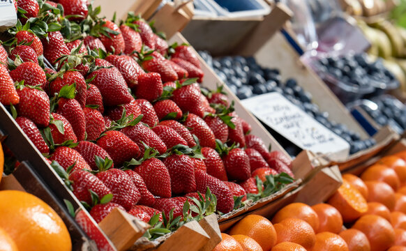 Fresh, ripe, large red strawberries with green leaves in a box neatly displayed on a counter at a street fruit and vegetable market. Close up.