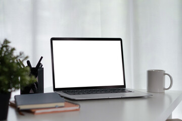 Fototapeta premium Laptop with Blank White Screen on Clean White Desk Workspace with Coffee Mug, Pens, and Plant