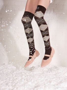 A pair of legs in long argyll socks jumps in the snow