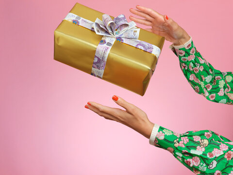 Hands catching a wrapped present with a bow made of money