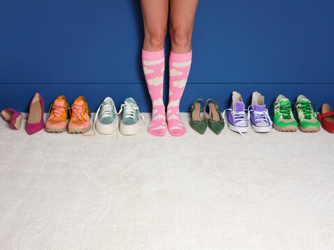 A women's legs in pink socks stands in amongst a row of shoes 