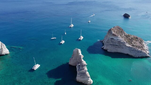 Sailboats enjoy a sunny day at Kleftiko bay in Milos, Greece, surrounded by white cliffs and blue waters