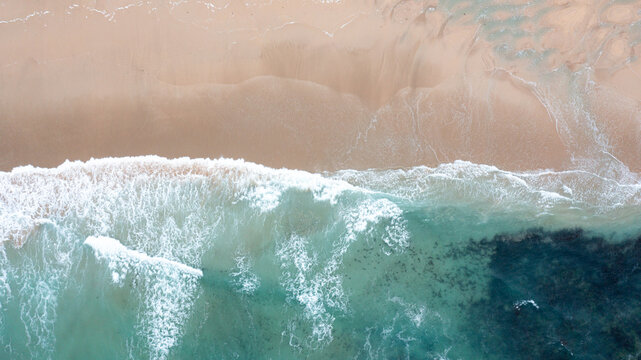 Aerial view of turquoise ocean waves crashing onto the sandy shore of Constantine Bay in Padstow, Cornwall, United Kingdom.