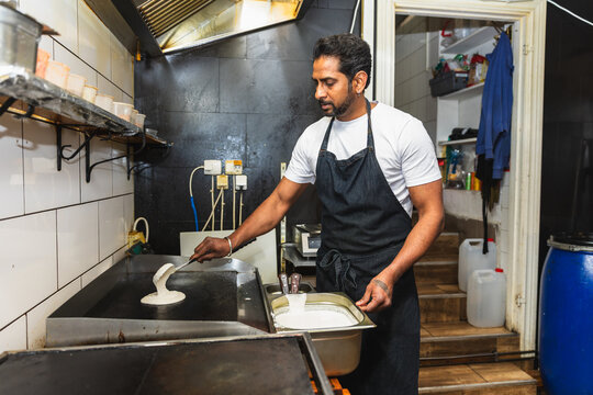 Chef pouring dosa batter on flat top grill