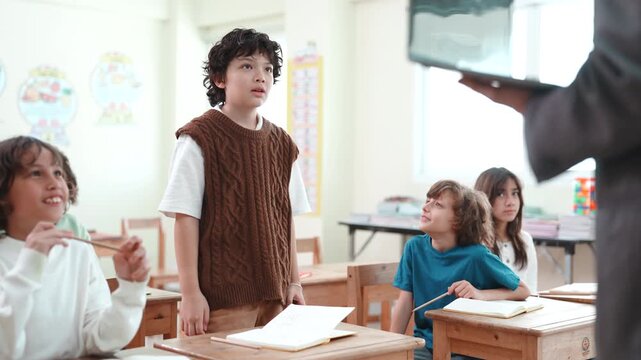 Confident boy standing and speaking in diverse classroom. Elementary school student giving a presentation or self introduction to teacher and classmates.