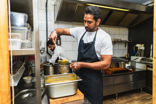 Indian chef pouring dal in commercial kitchen