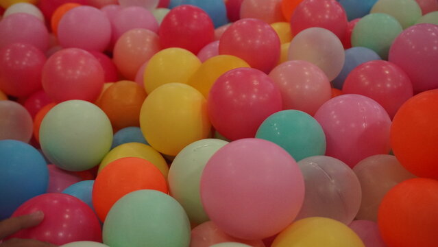 Pile of multicolored plastic balls in a kids ball pit, vivid pastel tones creating a fun cheerful texture.