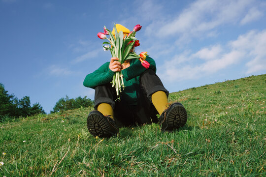 Person sitting on grass holding flowers in sunny outdoor scene