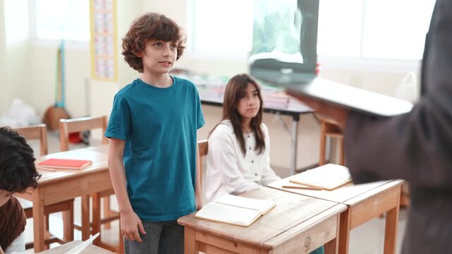 Confident boy standing and speaking in diverse classroom. Elementary school student giving a presentation or self introduction to teacher and classmates.