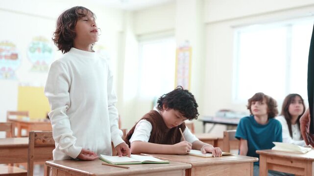 Confident young boy standing and giving a presentation in a primary school classroom. Student speaking or introducing himself to classmates during a lesson.