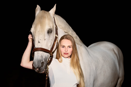 Woman Stands With White Horse in Dark Setting