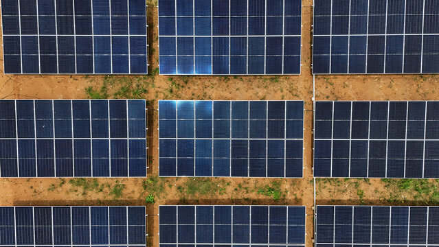 Aerial view of a solar panel array arranged in a grid pattern on reddish soil with sparse vegetation in Tanahgrogot, Kalimantan Timur, Indonesia.