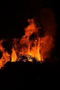 A massive traditional Judas burning bonfire lights up the night sky and a gathered crowd in Crete, Greece. Authentic Orthodox Easter cultural celebration at night.